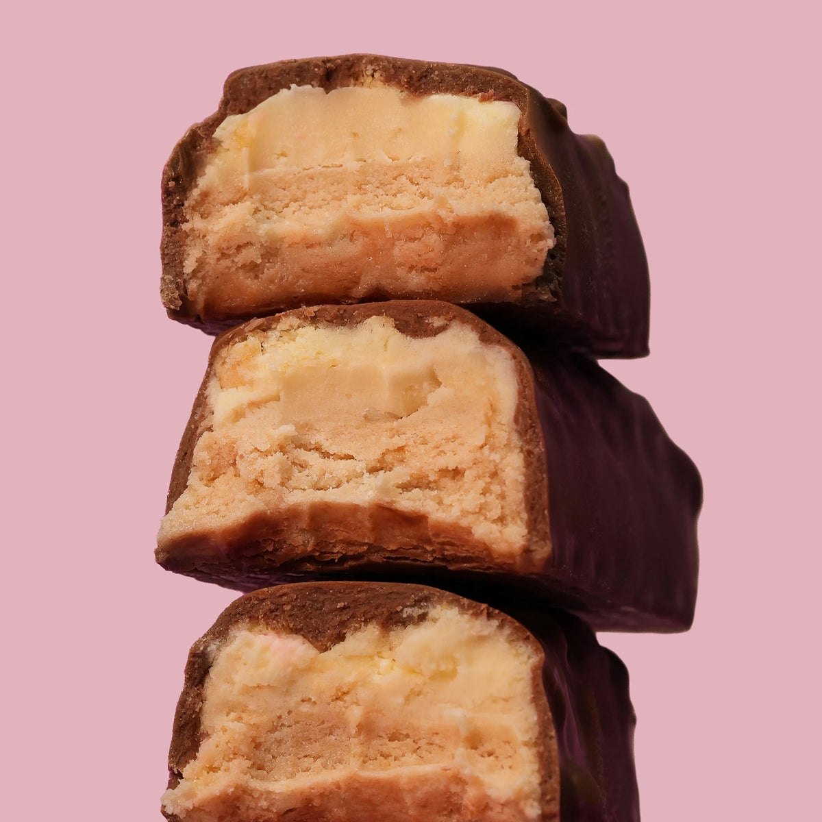 Three stacked chocolate-covered ice cream sandwich bars with creamy vanilla ice cream filling, set against a solid pink background.
