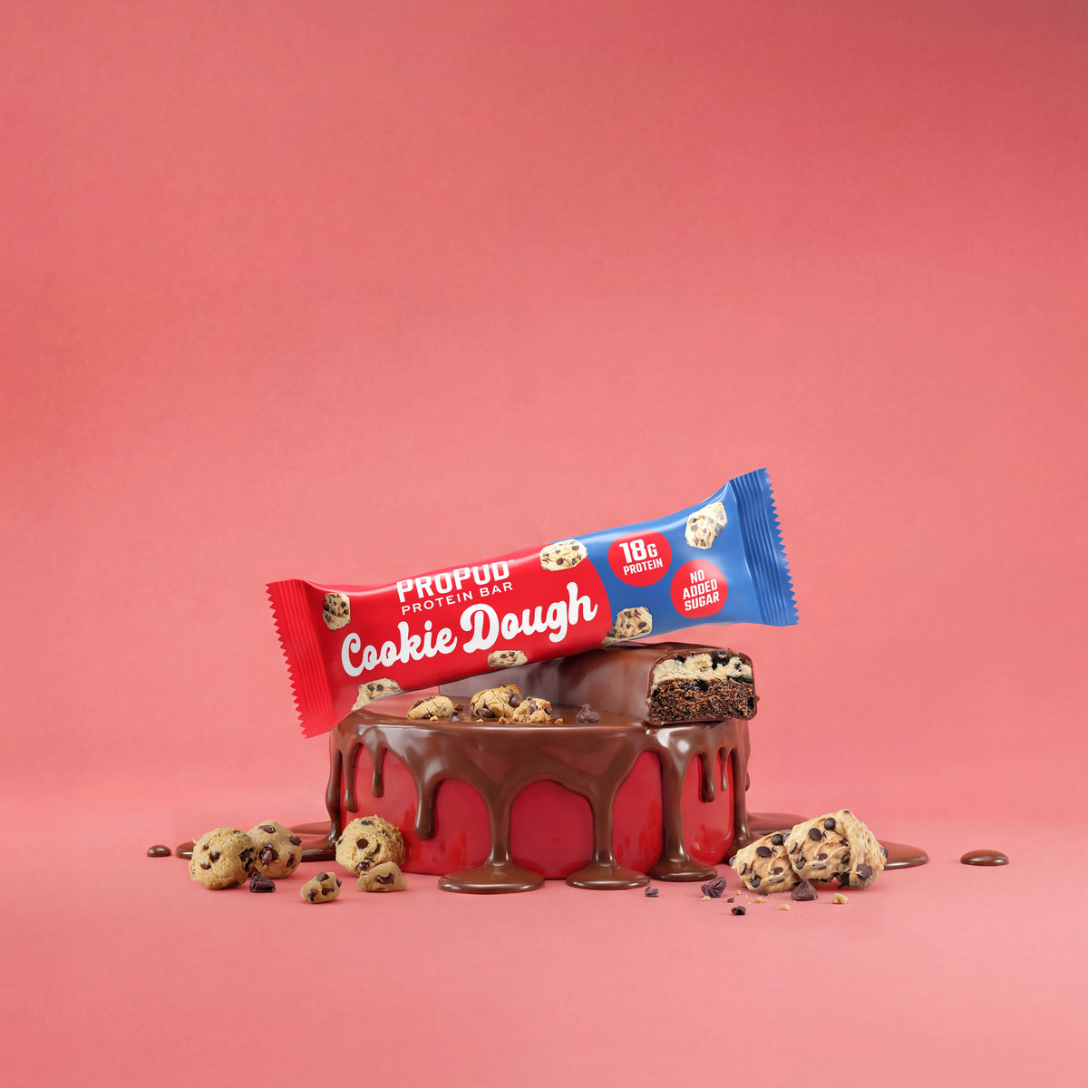 A ProPood Protein Cookie Dough protein bar, featuring a red and blue wrapper, is displayed on top of a chocolate-dripped red cake with cookie dough chips scattered around, set against a solid pink background.